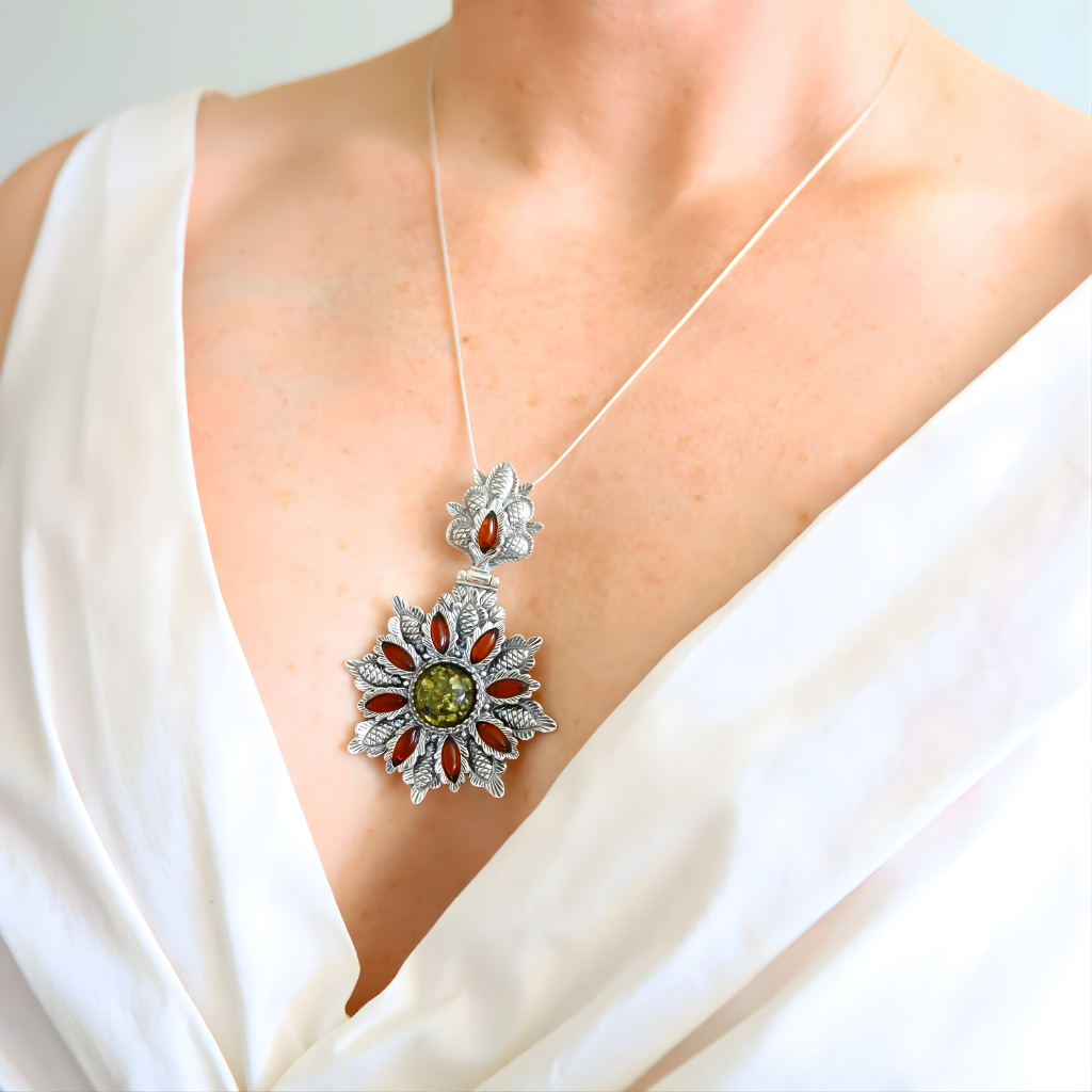 Silver necklace with green amber floral pendant featuring green and red stones on a white background
