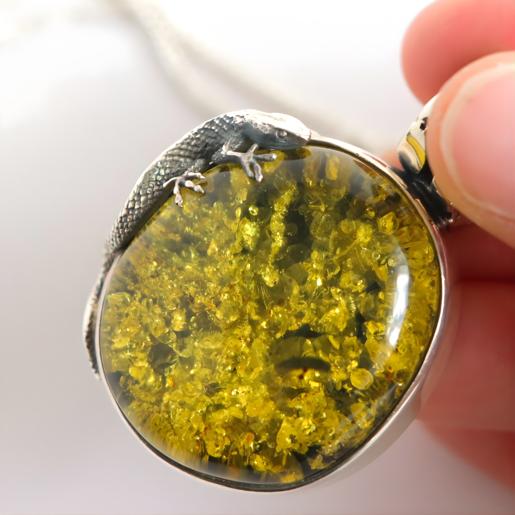 Close-up of a green amber pendant with a yellow stone and silver frame held by a hand.