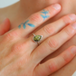Hand wearing a silver  amber ring with a green gemstone, with blue floral tattoos on the hand.