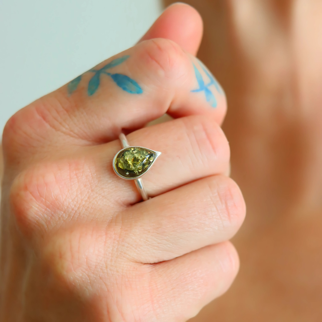 Hand wearing an amber ring with a green gemstone on a blurred background