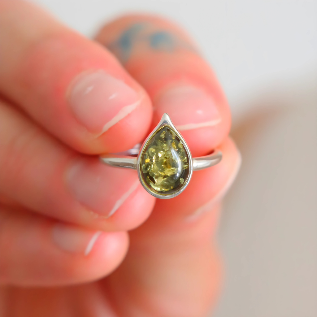 Teardrop-shaped gemstone amber ring on a finger with a blurred background