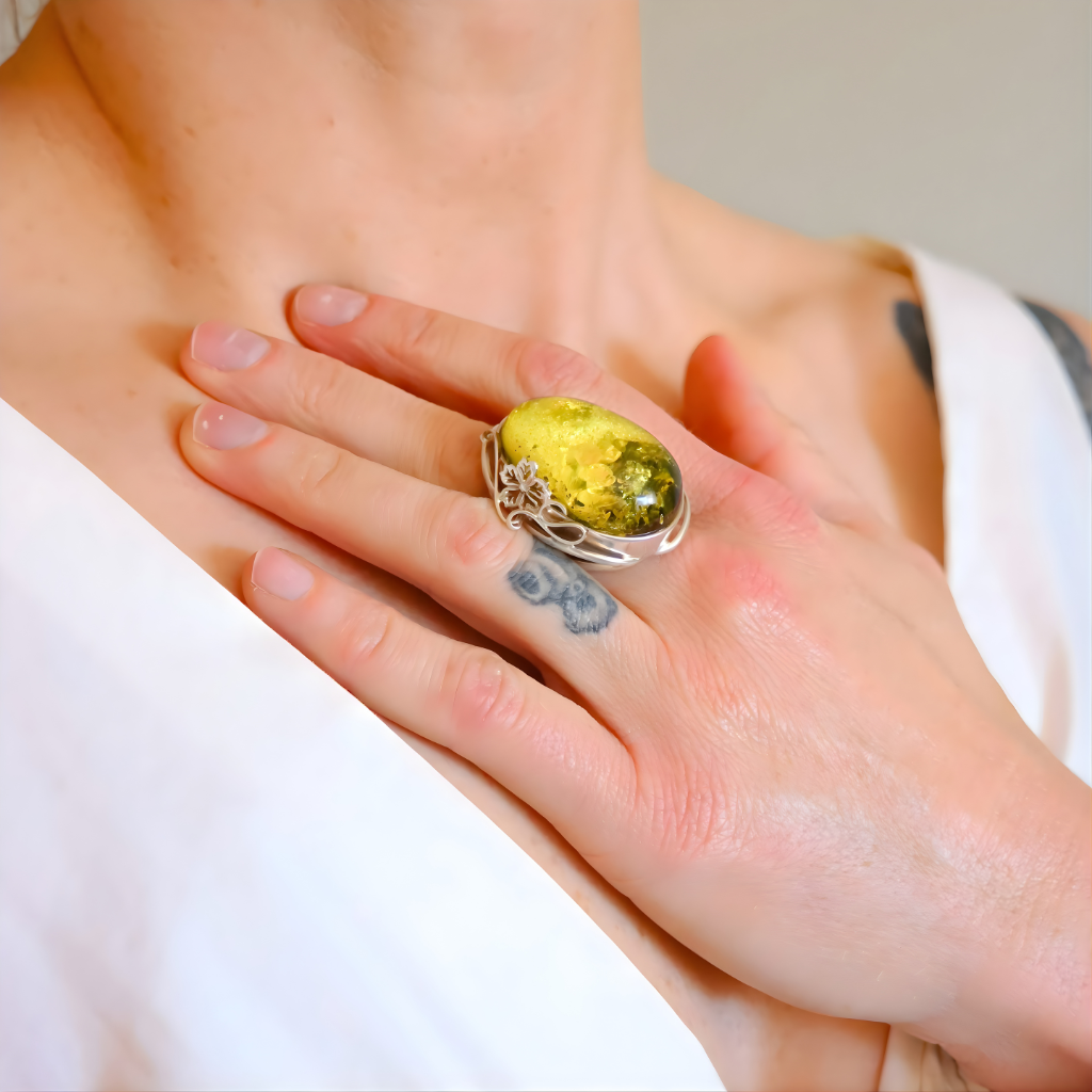 Hand wearing a sterling silver ring with a large green gemstone, held against a neutral background