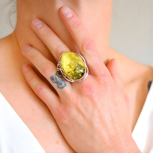 Hand wearing a sterling silver ring with a yellow stone on a neutral background