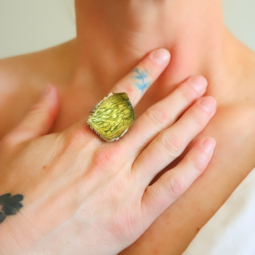 Close-up of a hand wearing a green amber ring with a textured surface.