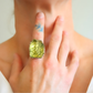 Close-up of a hand wearing a large green amber ring with a blurred background