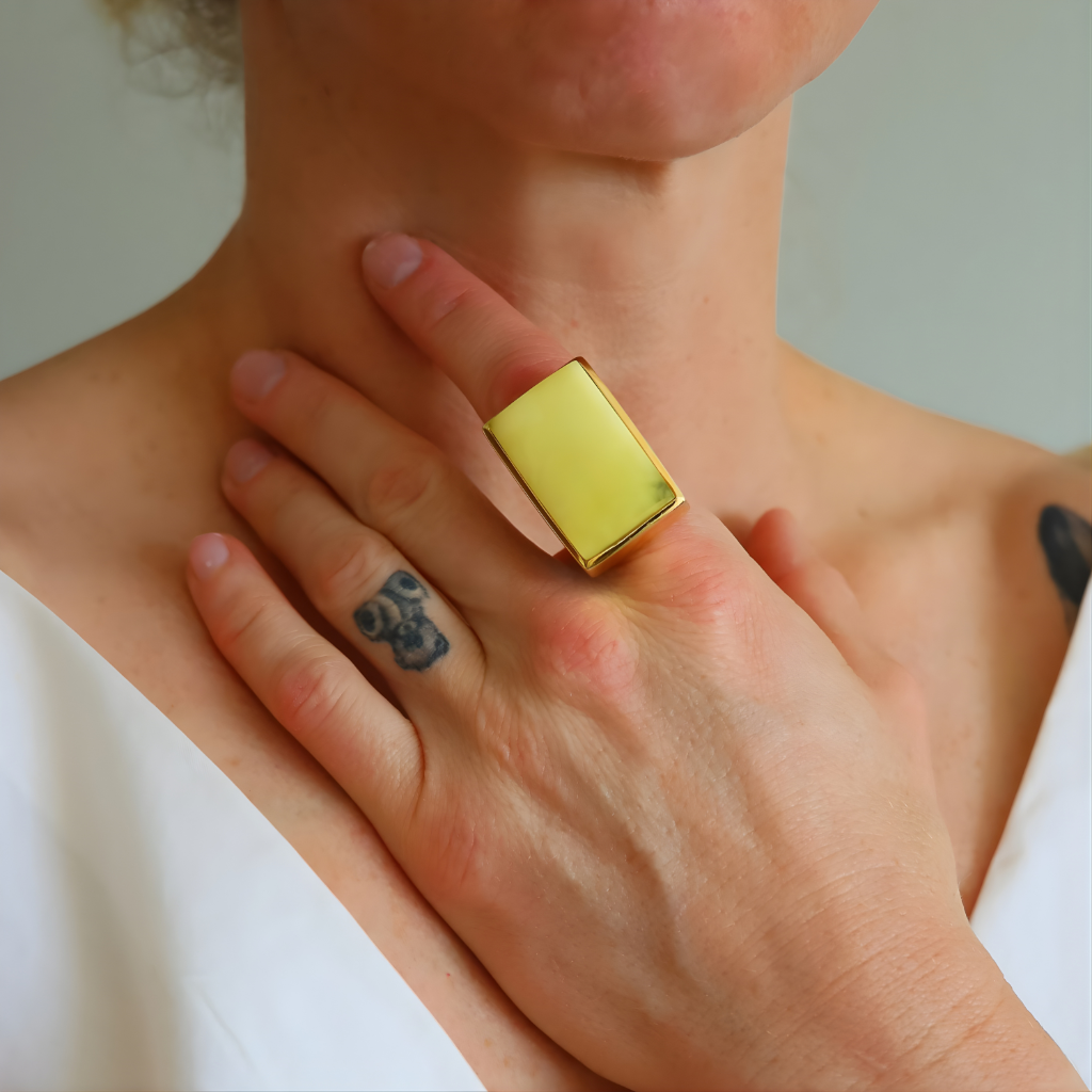 Person wearing a gold amber statement ring ring on a neutral background