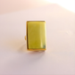 Gold amber statement ring with a rectangular green stone on a light pink background