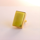 Gold amber statement ring with a rectangular green stone on a light pink background