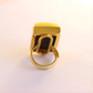Gold amber statement ring with a yellow gemstone on a light pink background