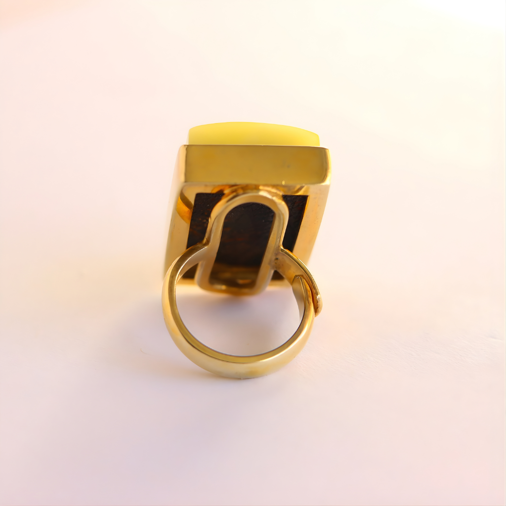 Gold amber statement ring with a yellow gemstone on a light pink background