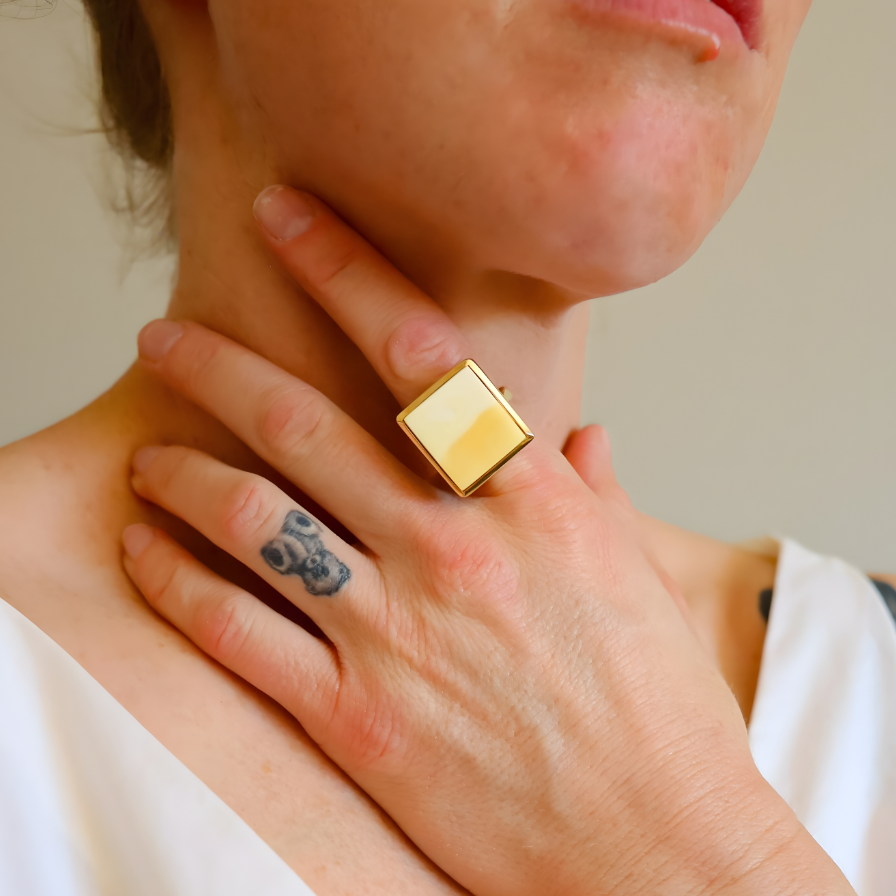 Person wearing a gold amber ring on their finger, with a neutral background