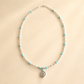 Turquoise necklace with blue gemstones and silver beads with silver concho pendant on light beige background