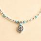 Turquoise necklace with silver beads and silver concho pendant on light beige background
