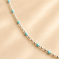 silver and turquoise necklace. small silver beads with round blue bead accents on light beige background