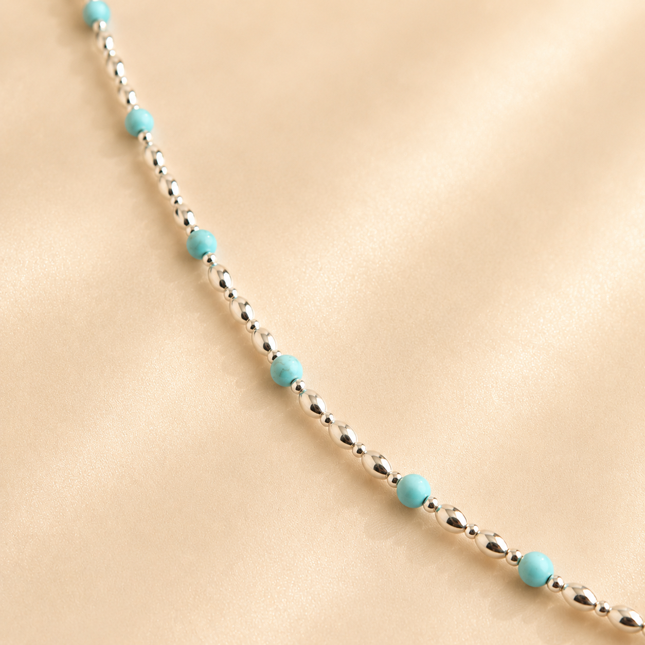 silver and turquoise necklace. small silver beads with round blue bead accents on light beige background