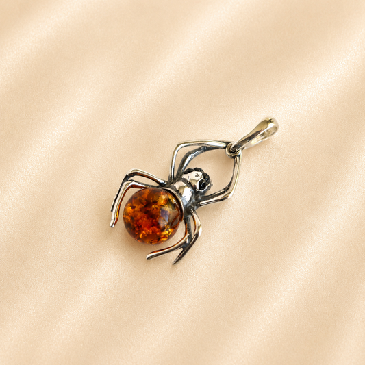 Amber Spider pendant with black eyes a orange gemstone and silver legs on light beige background