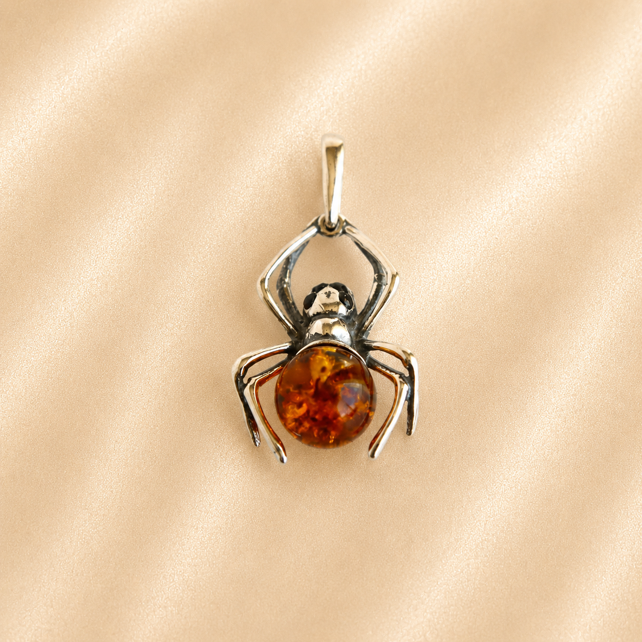 amber spider pendant with an orange gemstone silver legs and black eyes on beige pink background
