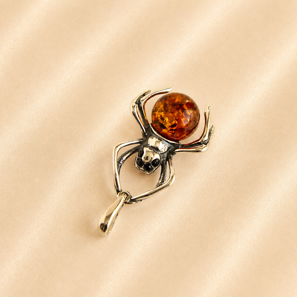 amber spider pendant with four black shiny eyes and orange gemstone on light beige background