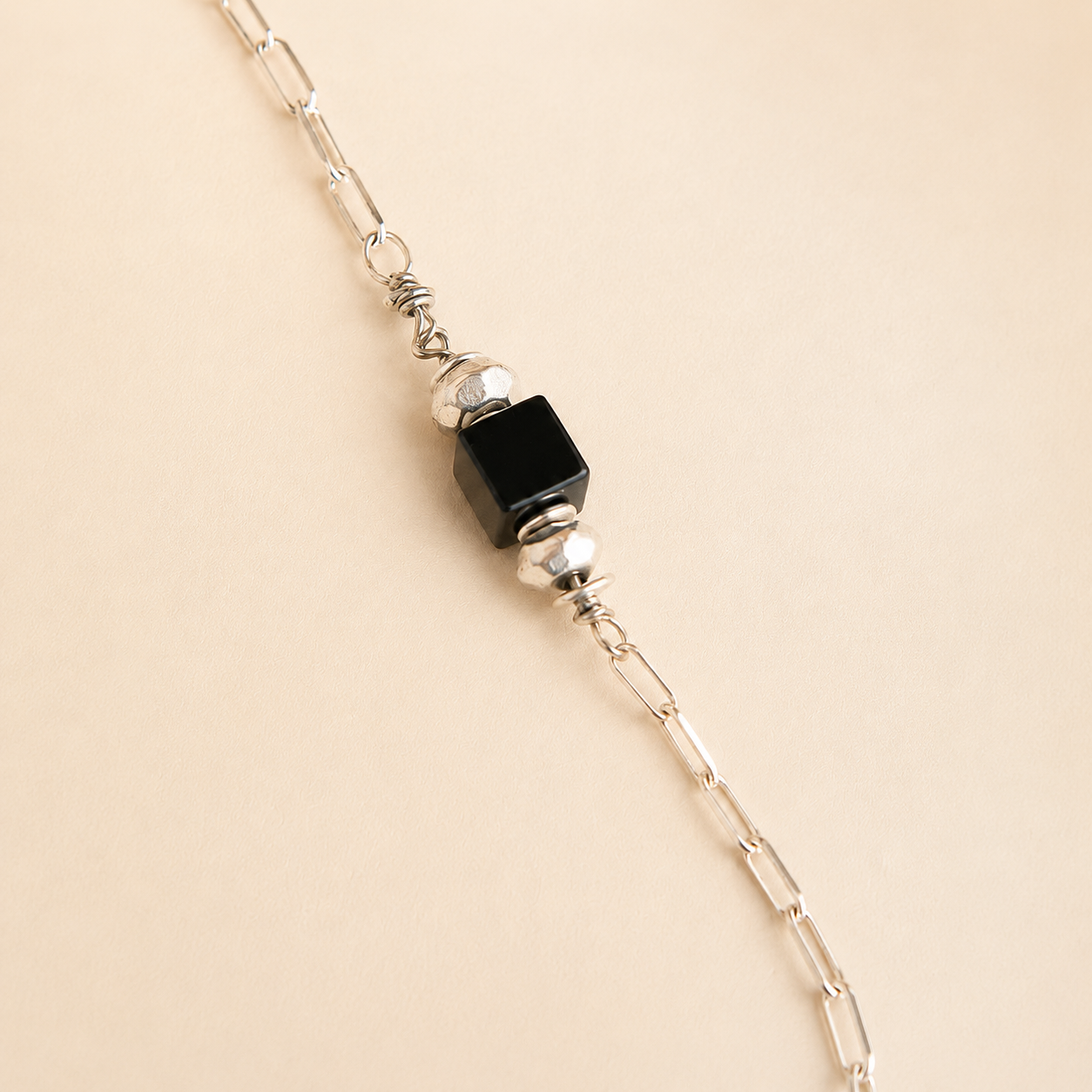 raven skull Necklace with black bead and silver chain on beige background