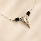 raven skull Necklace with a silver skull  pendant and black beads on a beige background