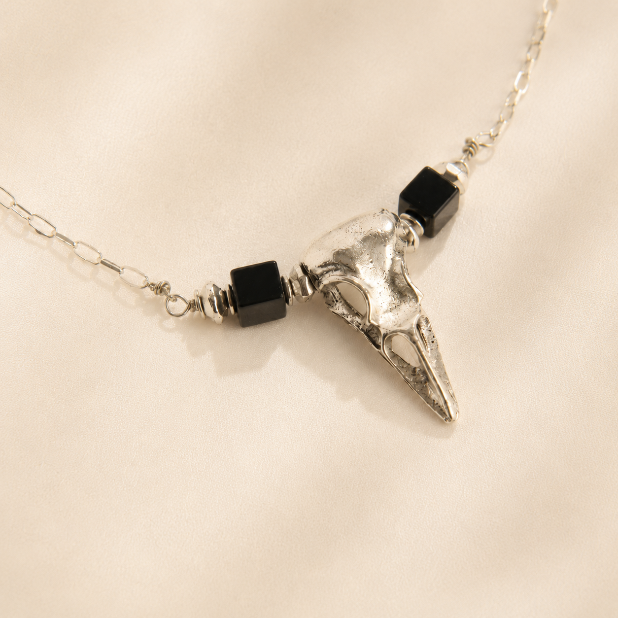 raven skull Necklace with a silver skull  pendant and black beads on a beige background
