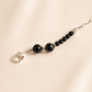 Black beaded raven skull necklace with silver clasp on a beige background