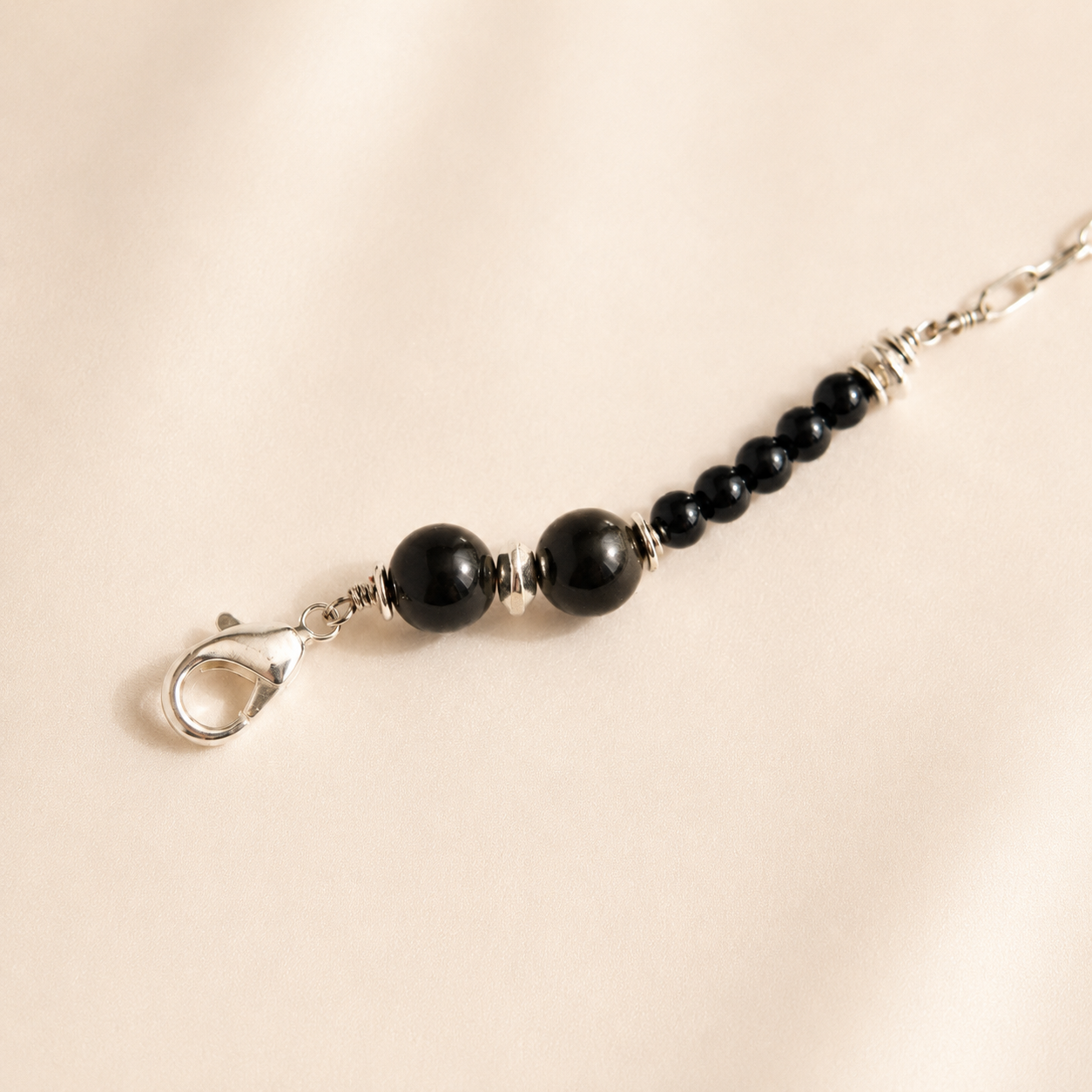 Black beaded raven skull necklace with silver clasp on a beige background