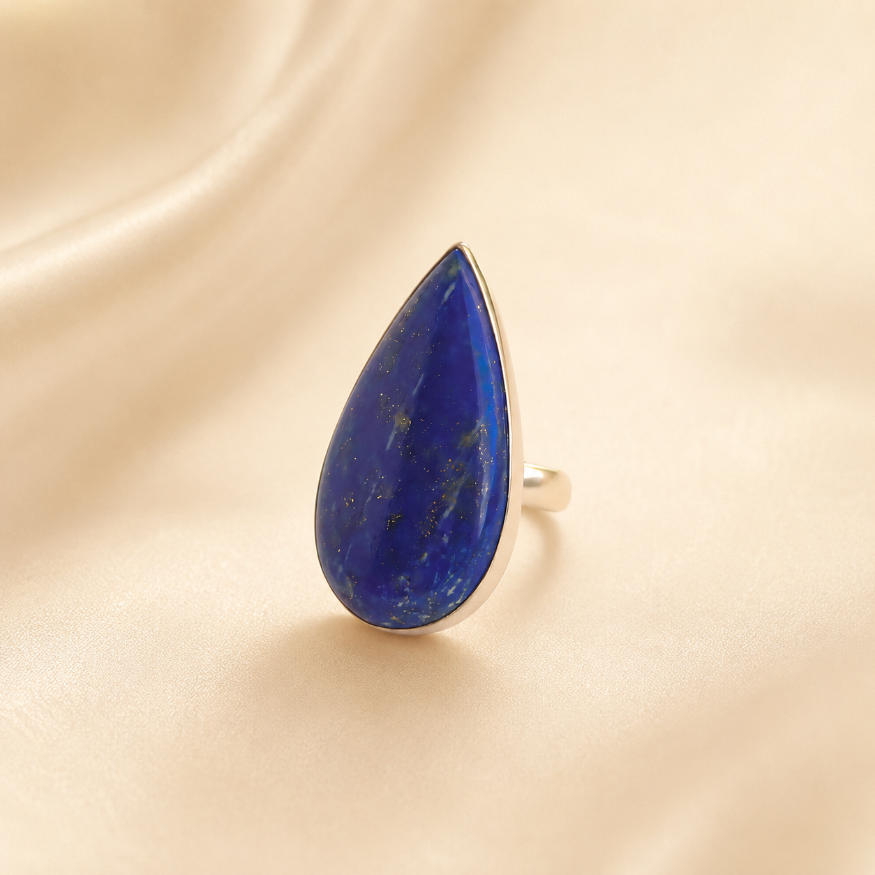 Teardrop-shaped lapis lazuli ring on a beige fabric background