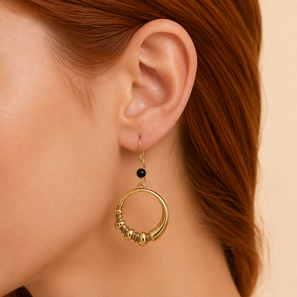 Gold hoop earring with beads worn by a person with red hair.