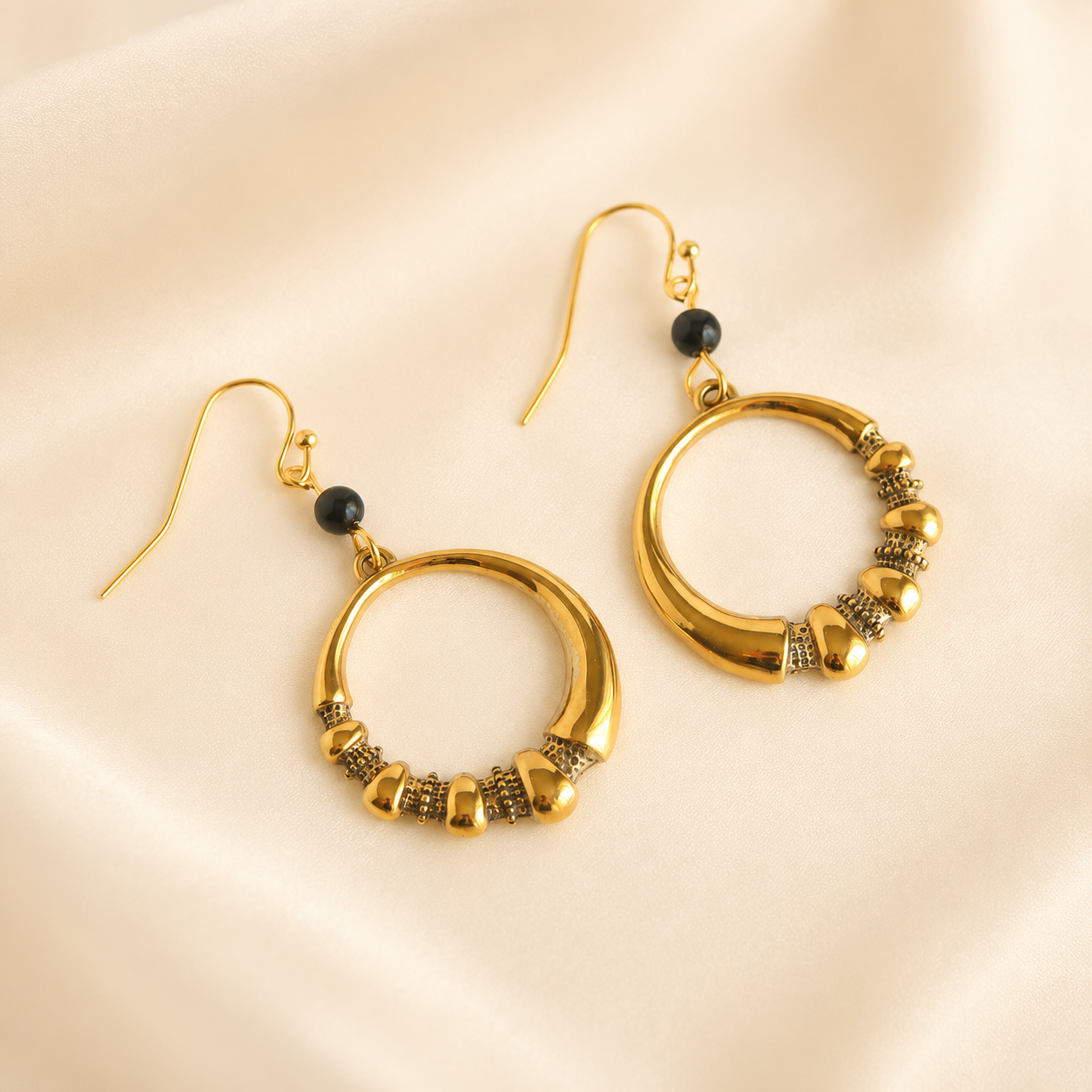 Gold hoop earrings with bead detailing on a beige background