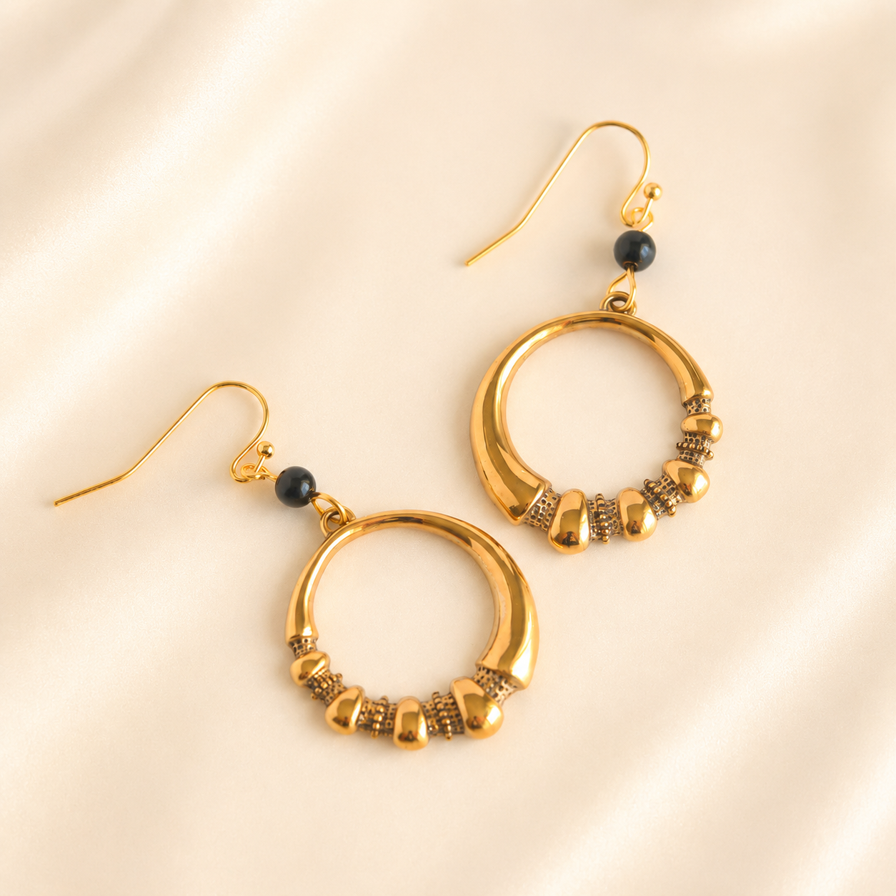 Gold hoop earrings with black beads on a beige background