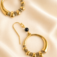 Gold hoop earrings with a black bead on a beige background