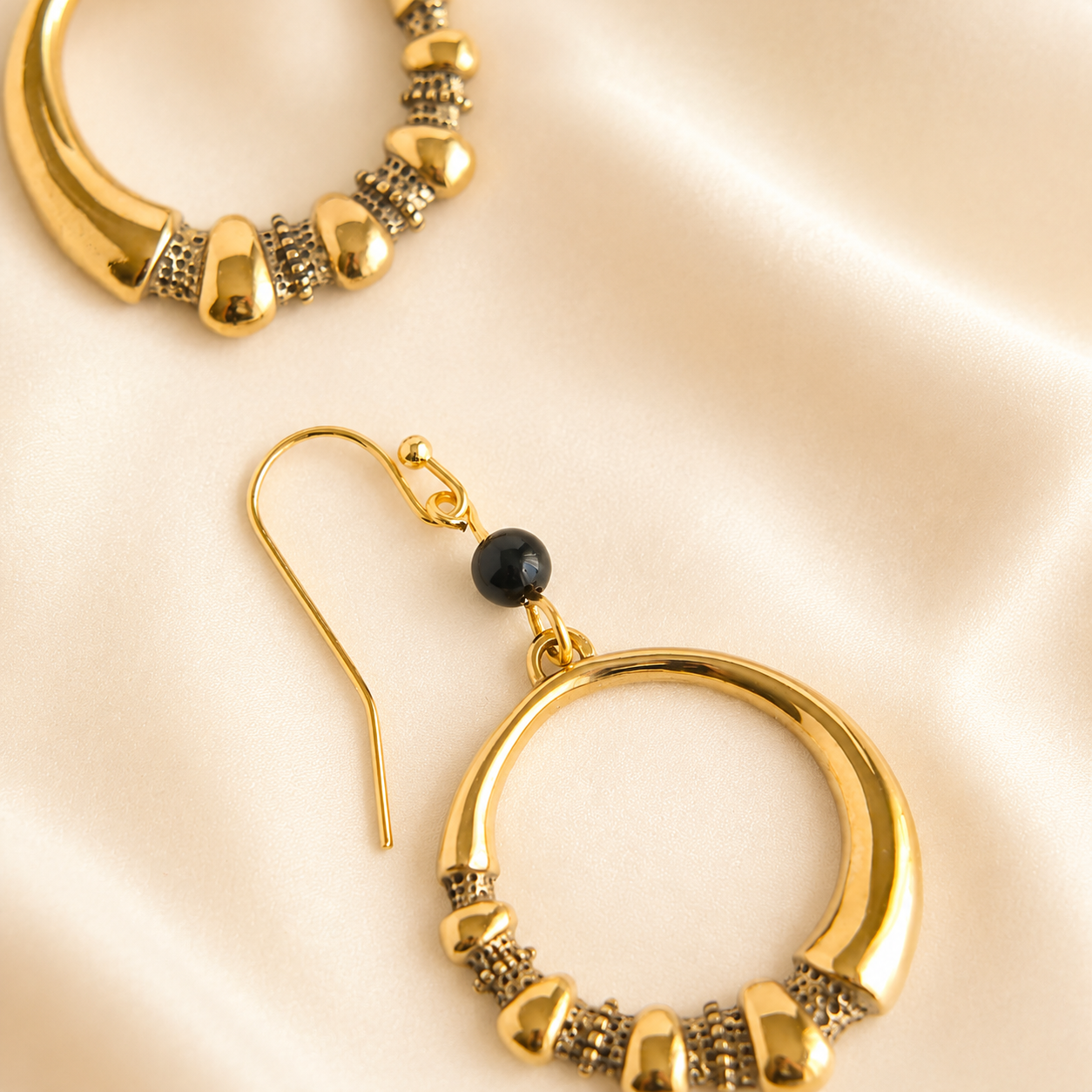 Gold hoop earrings with a black bead on a beige background