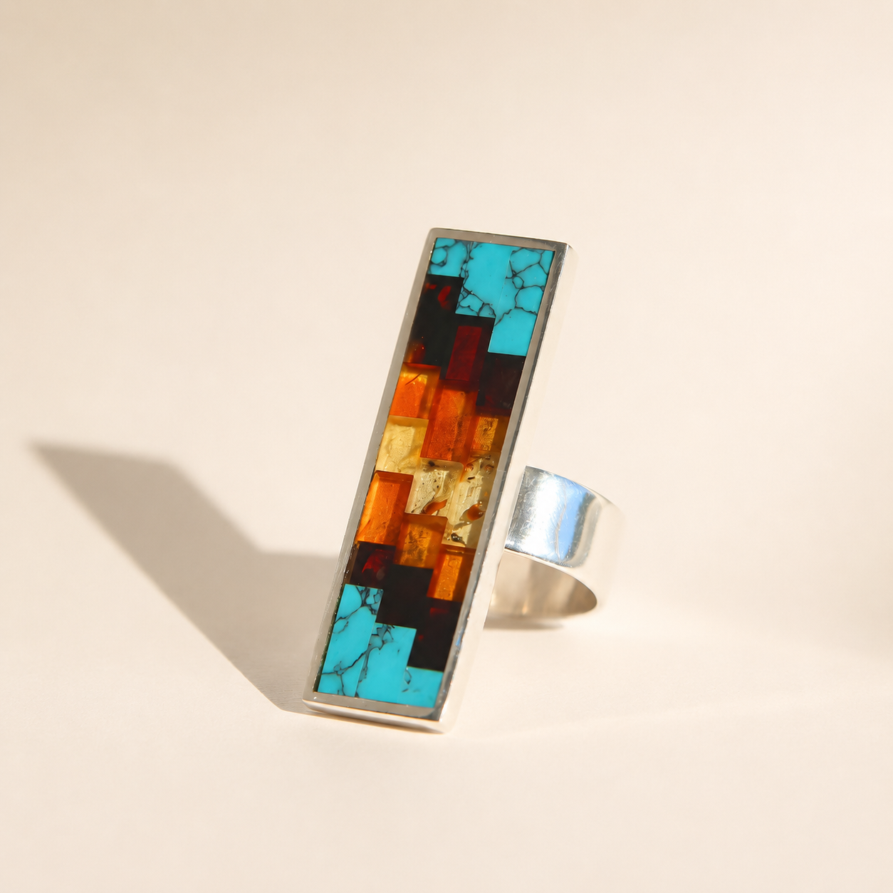 Silver amber ring with a colorful mosaic stone on a beige background
