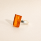 rectangular amber ring with orange gemstone on light beige background