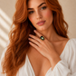 Woman with long red hair wearing a white top and a gold amber ring.