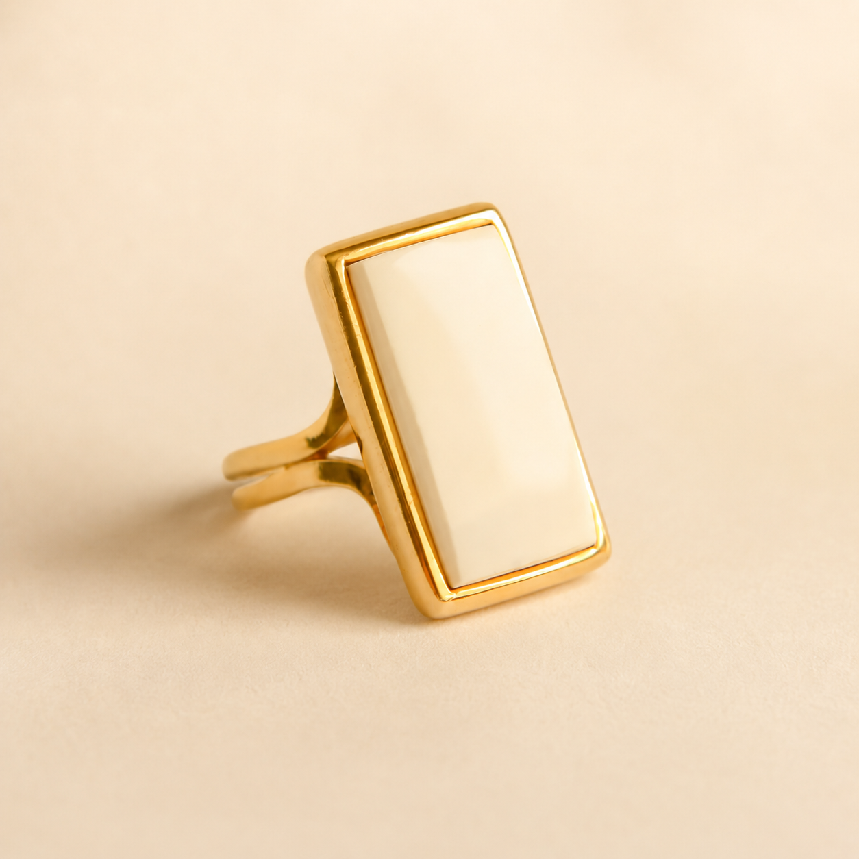 Gold white amber ring with a rectangular stone on a beige background
