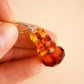 Close-up of a hand holding a silver drop earring  with amber-colored beads against a beige background