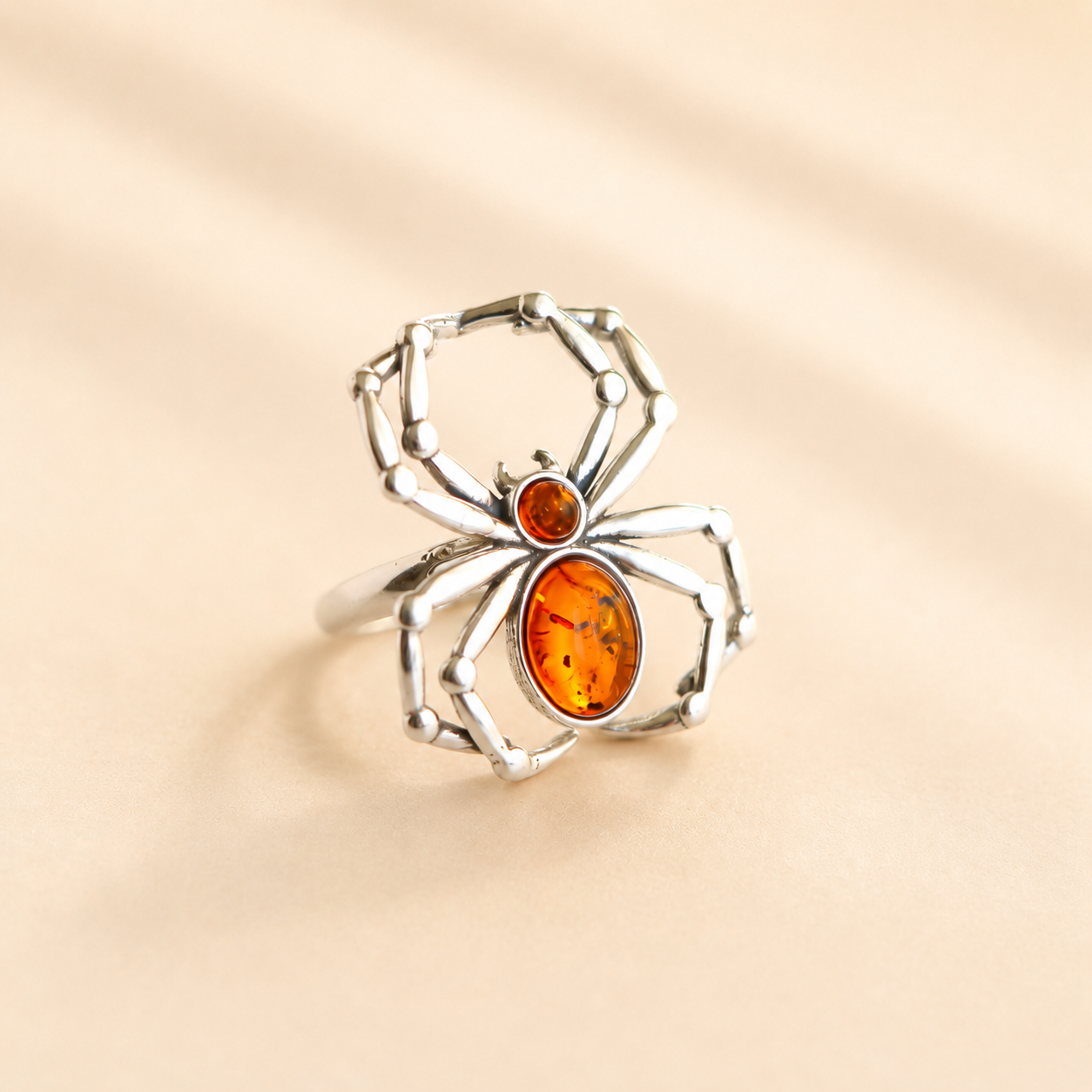 Silver spider amber ring with amber stones on a beige background