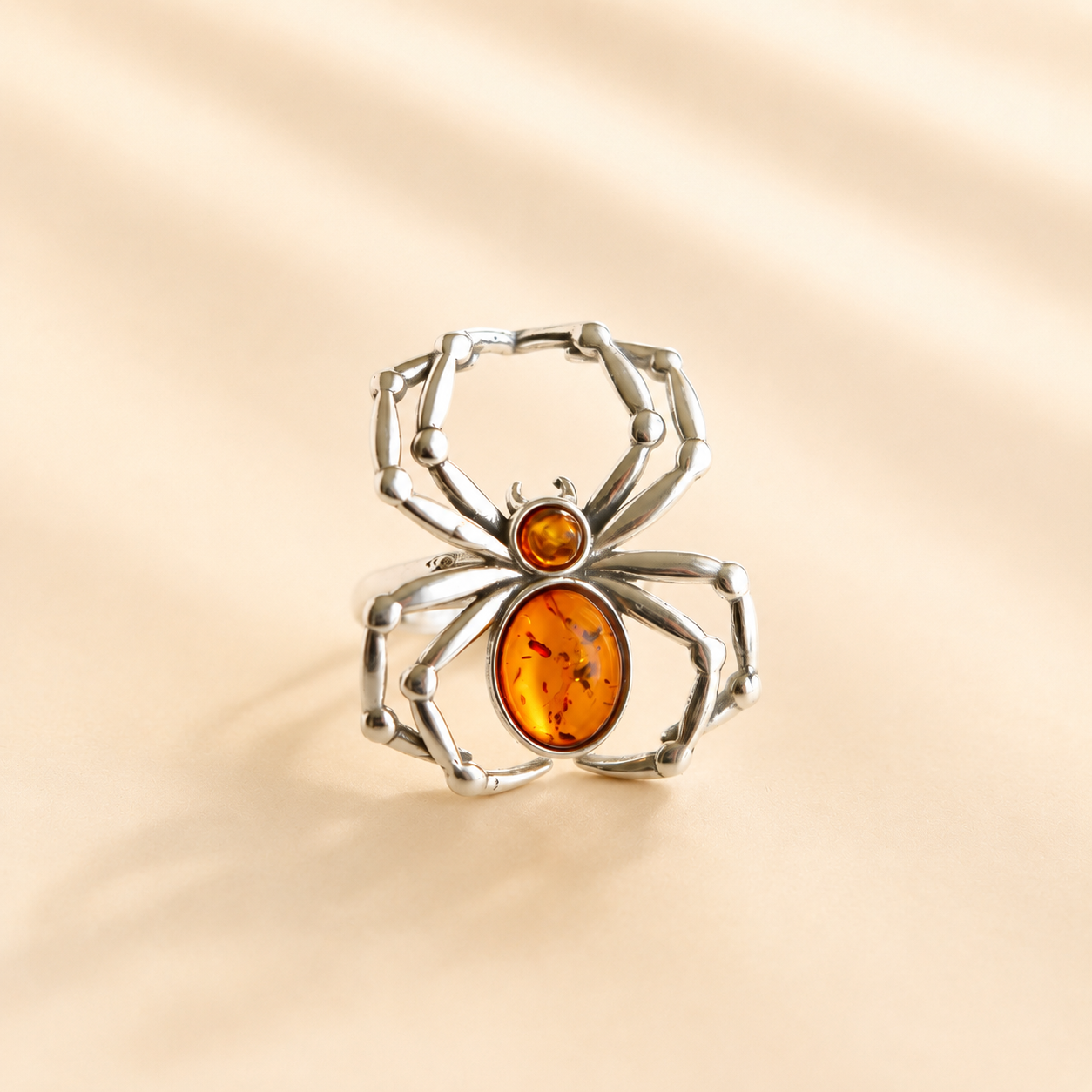 Silver spider-shaped amber ring with stones on a beige background