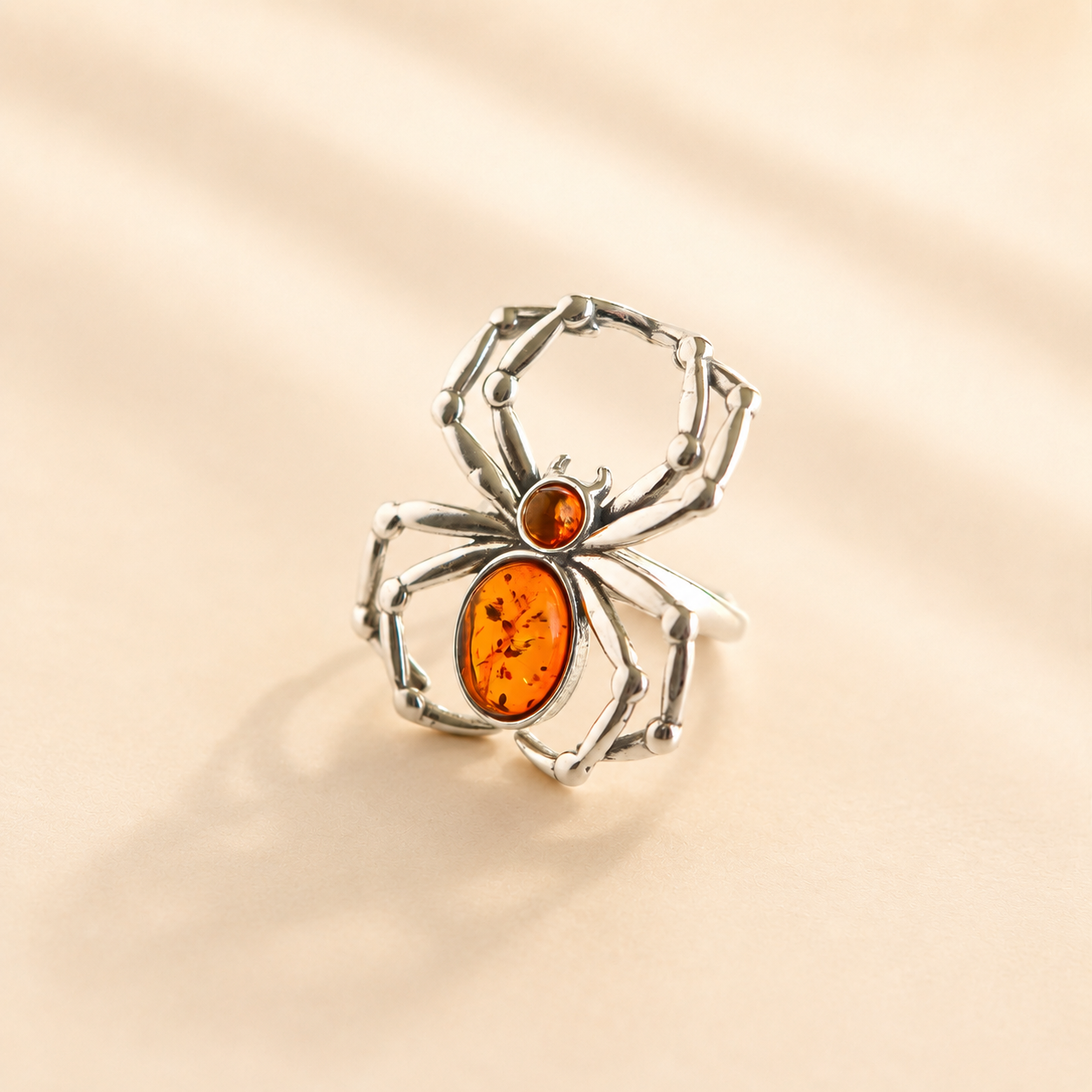 Silver spider-shaped amber ring with orange center on a beige background