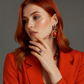 Woman wearing a red blazer, amber earrings, and a purple Solitaire ring on a gray background