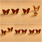 Butterfly gold stud earrings with red wings and gold bodies on a beige background