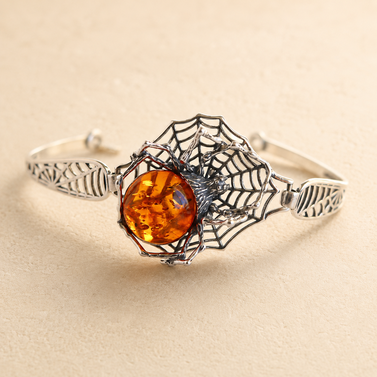 Silver amber bracelet with a spider web design and amber stone on a beige background