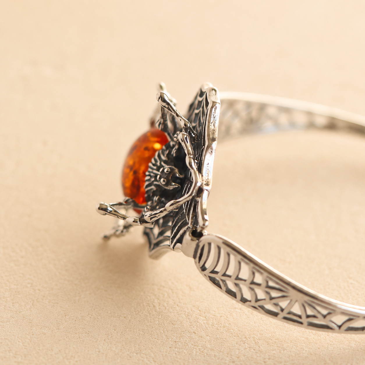 Silver spider amber bracelet with a red bead on a beige background