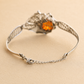 Silver amber bracelet with a heart-shaped orange gemstone on a beige background