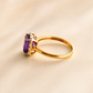 Gold Solitaire ring with a purple gemstone on a beige background