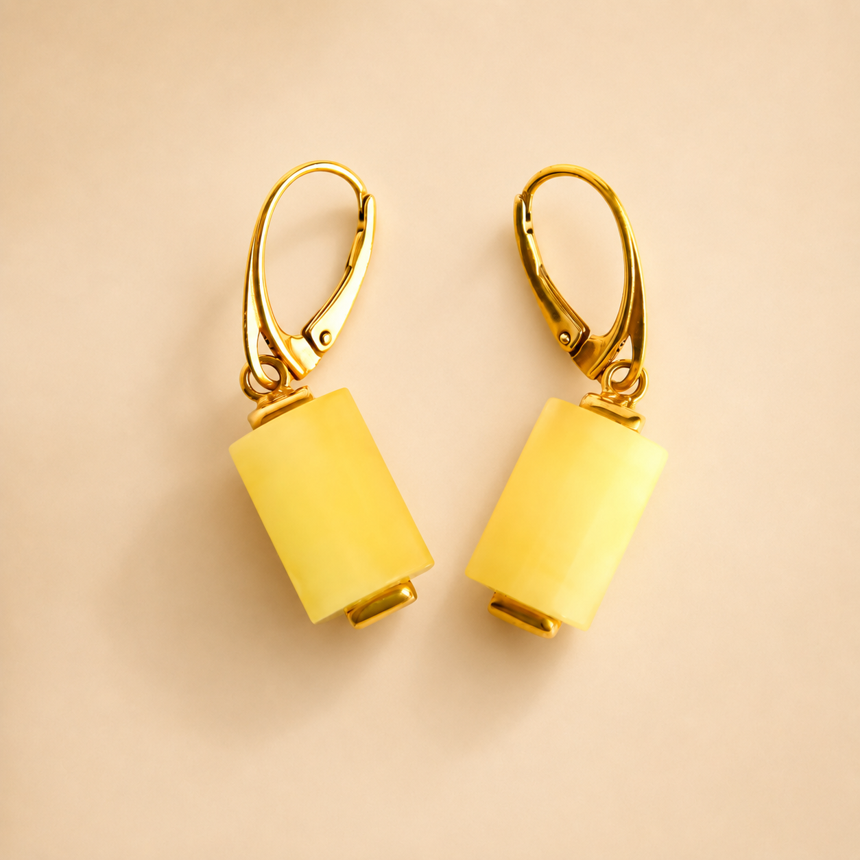Gold butterscotch amber earrings with yellow cylindrical pendants on a beige background