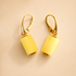 Gold butterscotch amber earrings with yellow cylindrical pendants on a beige background