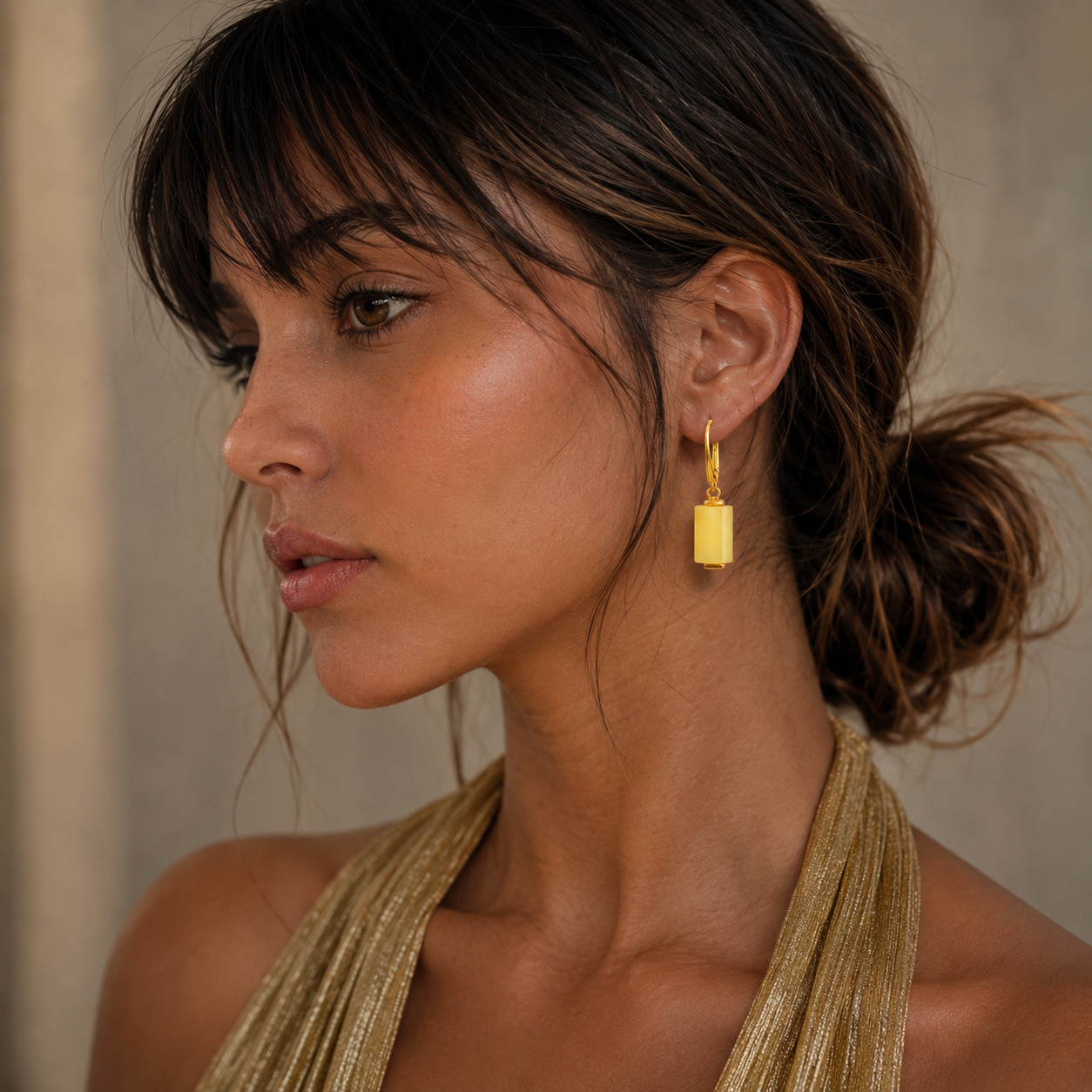 Woman wearing gold butterscotch amber earrings with a neutral background